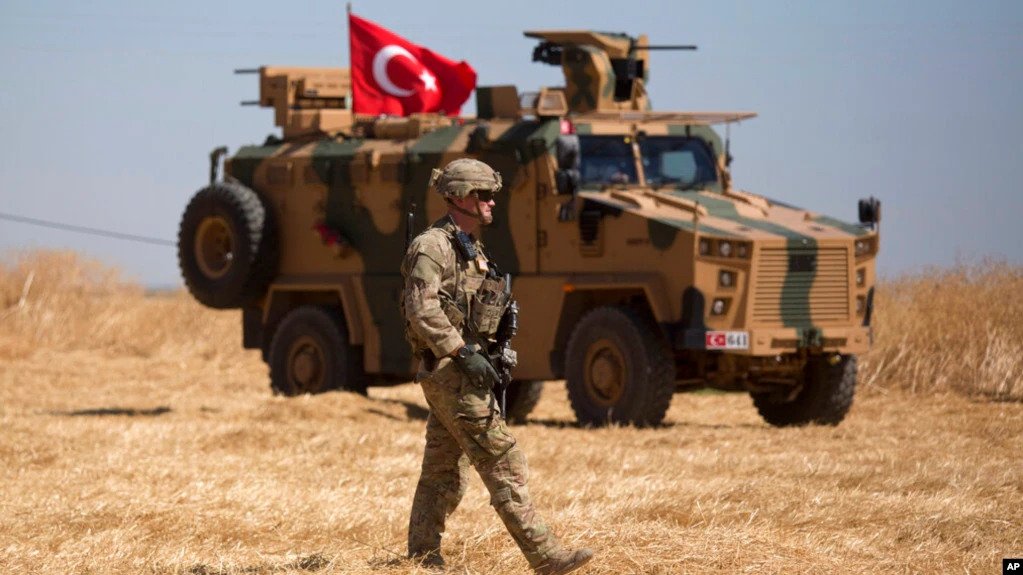 A U.S. soldier walks past a Turkish armored vehicle during the first joint ground patrol of American and Turkish forces in the so-called "safe zone" on the Syrian side of the border with Turkey, near Tal Abyad, Syria, Sept. 8, 2019.